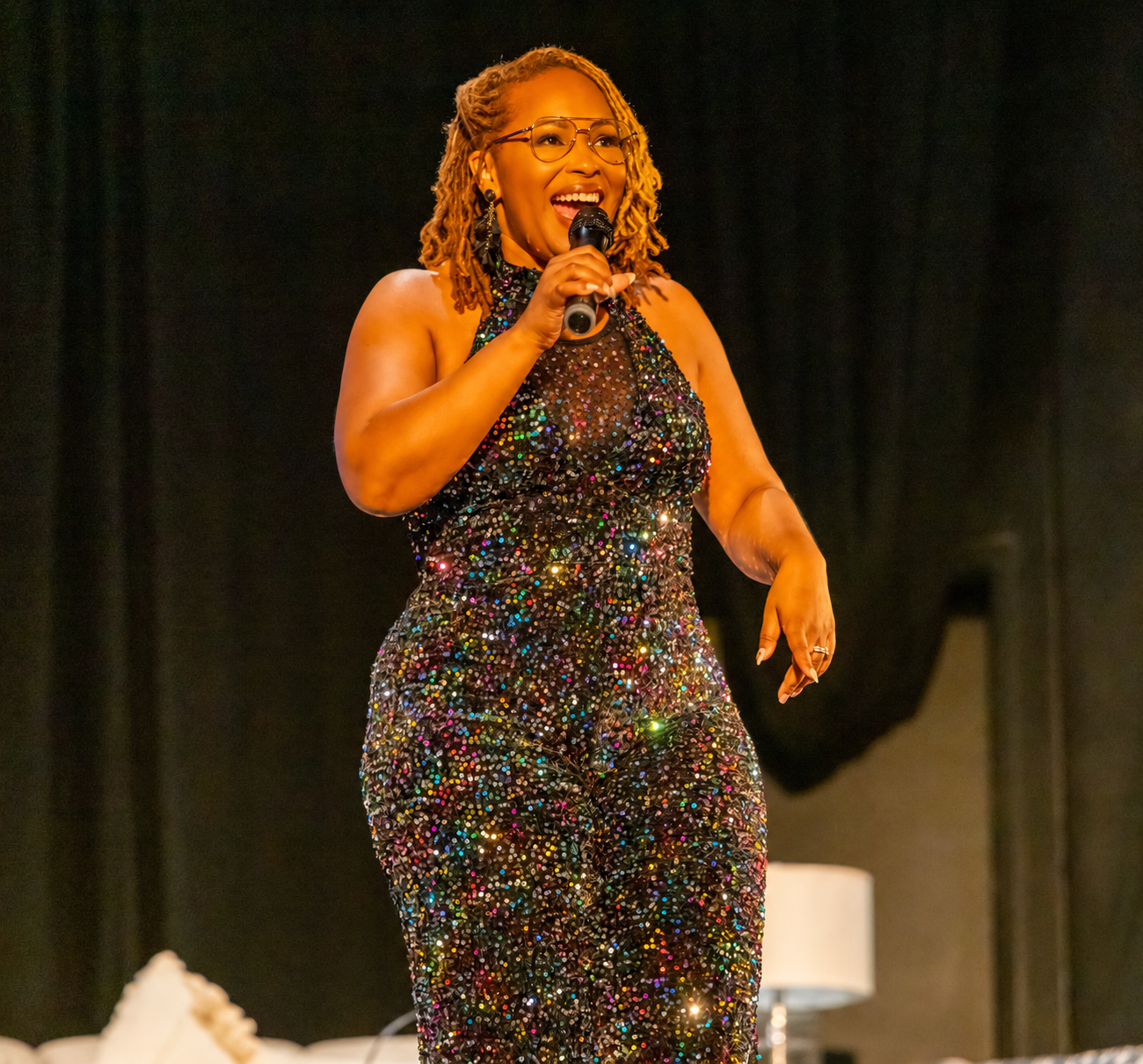Nikki speaking on stage in a sequined jumpsuit