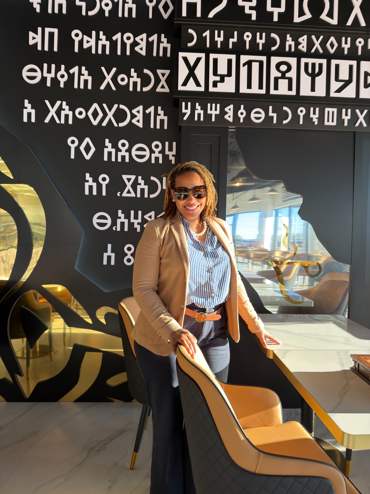 Nikki wearing a tan blazer and striped shirt in an artistic interior