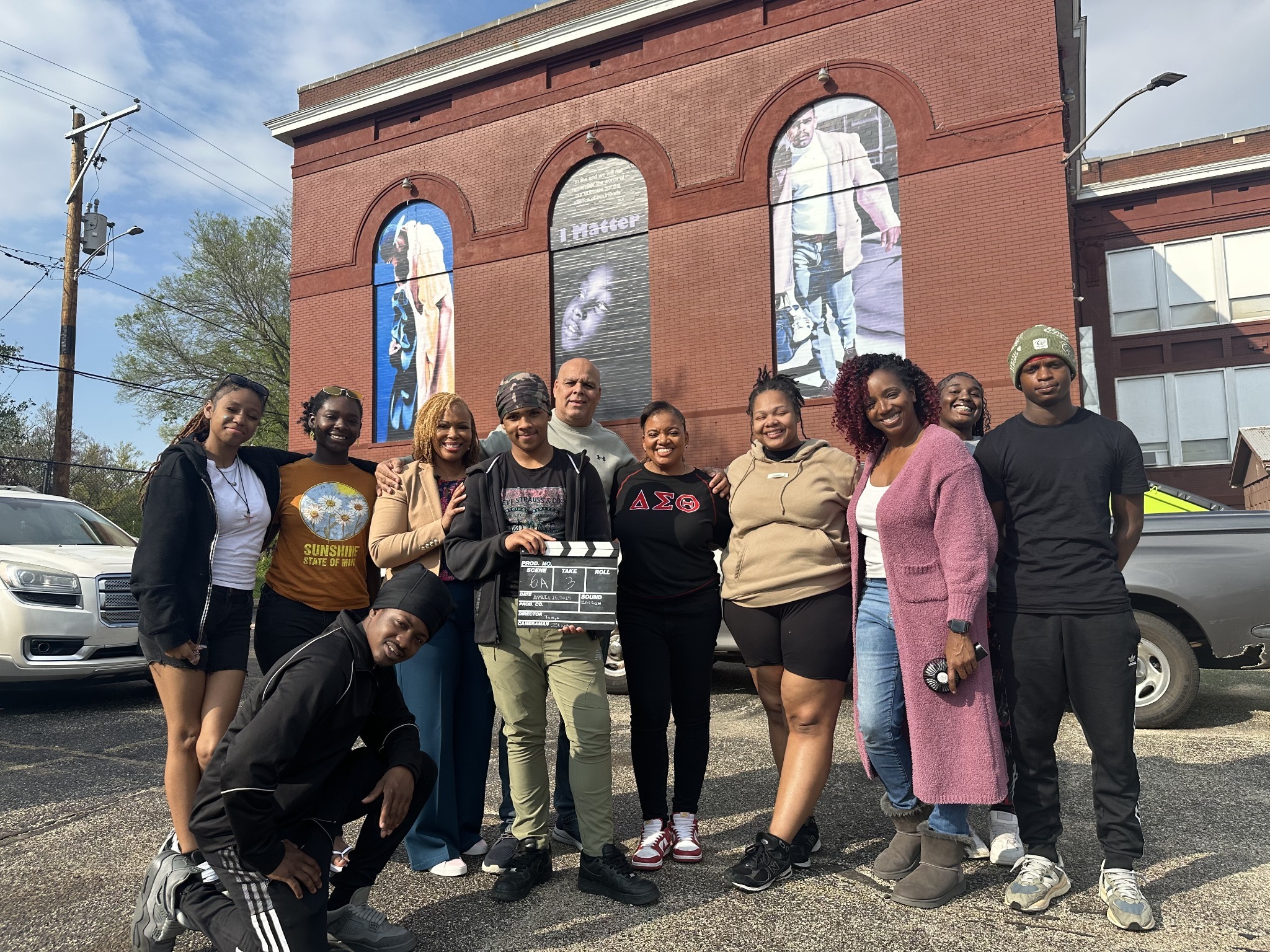 Nikki and Jonathon with a group of young people holding a film clapperboard outside ART INC